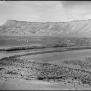 View of Palisade (Mesa County) Colorado; shows fruit orchards, farm land, residences and the Colorado River. The Book Cliffs and Mount Garfield are in the background.