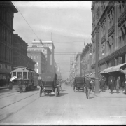 View of 16th (Sixteenth) Street in Denver, Colorado; shows automobiles, a horse-drawn carriage, bicyclists, pedestrians, an electric street car "Union Depot - #244," a clock,  Daniels & Fisher tower construction, and signs: "The Braman Co.," "A. J. Stark & Co.," and "A. T. Lewis & Son."