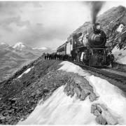 View of Denver, Northwestern & Pacific Railway (later called Denver & Salt Lake) engine number 100 & passenger train approaching Rollins Pass, Colorado; group of people standing beside standard gauge track & train, snowfields; Moffat Road, Continental Divide; Rocky Mountains, background left .