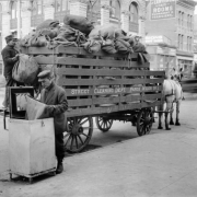 View of men working and a horse drawn-trash collection wagon on Arapahoe Street, in Denver, Colorado; brick and stone businesses are in the background. Lettering reads: "Street Cleaning Dept. Paper Wagon No. 1."