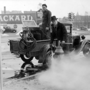 View of men working with a truck and spray-cleaning compressor, washing a fire hydrant in Denver, Colorado. A traffic signal is in the background.