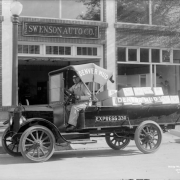 A man sits in a delivery truck parked near the Swenson Auto Company at 1960 Champa Street in downtown Denver, Colorado. Lettering on the truck reads: "Denver Mud Express 330."