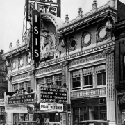 View of the Isis Theater at 1722 Curtis Street in downtown Denver, Colorado. Automobiles are parked near the three-story building with an ornate theater facade. Signs read: "William Fox Isis," "James Cagney in 'G Men' Jessie Matthews in Evergreen," "Mickey Mouse Cartoon," and "Baer-Louis Fight Returns Round by Round."