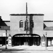 View of the Mission Theater at 1465 South Pearl Street in the Platt Park neighborhood of Denver, Colorado. The two-story building has a tile roof and arched window wells. Signs read: "Mens Suits Overcoats Dresses Plain Ladies Coats," "The Man I Love With Mary Brian & Richard Arlen Also Comedy," and "Always the Best Show in South Denver."
