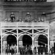 Men and women pose outdoors near the Palace theater at 15th (Fifteenth) and Blake Streets in downtown Denver, Colorado. One group of men and women pose on the balcony on the second floor of the theater.