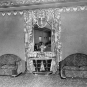 View of the foyer of a balcony in the Paramount Theater designed by Temple Hoyne Buell in Denver, Colorado. A statue of a woman in lotus position is on a table. A mirror and drapes are on the wall near a set of love seats.