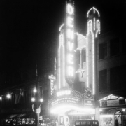 Night view of the 16th street entrance of the Denver Theater at 510 16th (Sixteenth) Street in Denver, Colorado; shows electric signs and the marquee: "Joan Crawford in Modern Maidens," and "Ted Hack in Say It With Music." Banner reads: "Cuba - U.S.A."