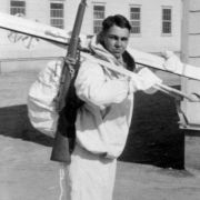 John D. Magrath, a member of the 10th Mountain Division 85th Regiment, Company G and a recipient of the Congressional Medal of Honor, poses outdoors with skis and poles at Camp Hale (Eagle County), Colorado. He wears a backpack with rifle, jacket, and mittens.