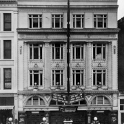 Rooftop view of the Rialto Theater at 1540 Curtis Street in downtown Denver, Colorado. The four-story building has ornate trim and is decorated with electric lights. The marquee reads: "Jack Holt and Agnes Ayres in Bought and Paid For."