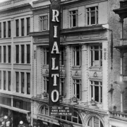 Rooftop view of the Rialto Theater at 1540 Curtis Street in downtown Denver, Colorado. The four-story building has ornate trim and is decorated with electric lights. The marquee reads: "Jack Holt and Agnes Ayres in Bought and Paid For."