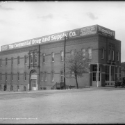 Drug store in Denver, Colorado; signs read: "Tonics, Feeds, Farm Remedies, Serums, Vaccines, Disinfectants- The Centennial Drug and Supply Co.- Stock, Poultry Supplies and Specialties, Veterinary Instruments... Founded 1912." A car is on Walnut Street.