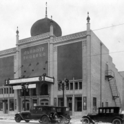 View of the Aladdin Theatre (with Moorish arches and onion dome) at 2010 Colfax Street, in Denver, Colorado;  also shows streetlamps and cars. Marquee reads: "Monte Blue - Wolf's Clothing."