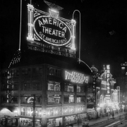 Nighttime view of the America theater at Curtis and 16th (Sixteenth) Streets in Denver, Colorado; shows storefronts, a popcorn cart, and electric signs: "America Theater - Mary Maclane in Men Who Have Made Love To Me," "Greater Vitagraph Photoplays," and "Empress."