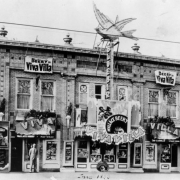 View of the Bluebird Theater at 3317 East Colfax Street in Denver, Colorado; electric sign depicts a bird and reads: "Bluebird," banners read: "Wallace Beery in Viva Villa." Corbeled brick and urns ornament the building.