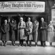 Group portrait of the Abbey Theatre Irish Players in Denver, Colorado; shows men and women in winter coats. The Broadway Theater entrance is in the background.