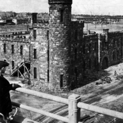 A boy with a bicycle stands on the 16th (Sixteenth) Street Viaduct near Walker Castle (Castle of Culture and Commerce) in Riverfront Park, Denver, Colorado. The stone castle has a round turret and battlements.