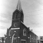 View of Saint Joseph Polish Church at 517 East 46th (Forty-sixth) Avenue in the Globeville neighborhood of Denver, Colorado. The brick building has a bell tower, spire, and circular and arched stained glass windows. A banner reads (in Polish): "Kosciol Sw Jozefa."