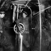 Two miners working by candlelight tend a diamond drill rig one mile underground in the Camp Bird mine, Ouray County, Colorado.