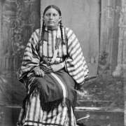Studio portrait (sitting) of George Bent's wife Magpie, a Native American (Cheyenne) woman. She wears beaded moccasins, a fringed blanket, and bead necklaces.