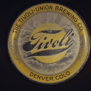 View of  a beer cap (ca.1901-1915) from the Tivoli-Union Brewery in Denver, Colorado. Shows a gold colored bottle cap with a central image of the sun and rays that radiate outward on a field of gray clouds. The words: "Trade Mark" and "Tivoli" are superimposed over the sun. The cap has a gold rim with Art-Nouveau designs and the words: "The Tivoli-Union Brewing Co., Denver, Colo."