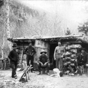 View of five miners and dog at log cabin with dirt roof, Colorado.