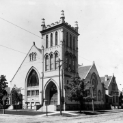 View of the First Avenue Presbyterian Church at 120 West First Avenue in the Baker neighborhood of Denver, Colorado. The brick church has a bell tower with arched windows and battlements, stained glass windows, and an arched entryway.