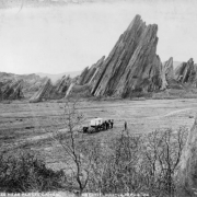 View of a mule drawn wagon with supplies set behind it, possibly the photographer's, near large jagged sandstone rock formations in what is now Roxborough State Park, Douglas County, Colorado. Shows a man by the wagon; two men pose by a small rock formation in the foreground.