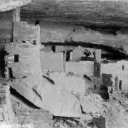 A man poses in Cliff Palace, a Native American (Anasazi) cliff dwelling at Mesa Verde National Park, in Montezuma County, Colorado. Shows masonry ruins and a stone overhang.