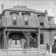 View of the George W. Kramer home at 2445 California Street in the Five Points neighborhood of Denver, Colorado; features a mansard roof, terrace, and covered porch. Women pose with a boy and a dog.