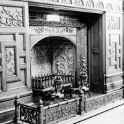 Interior view of a fireplace in the dining room of the David Moffat house at 808 Grant Street in the Capitol Hill neighborhood of Denver, Colorado. A decorative wooden mantle and metal grates are nearby.