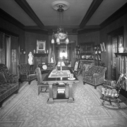 Interior view of the library at the David H. Moffat house at 808 Grant Street in the Capitol Hill neighborhood of Denver, Colorado. A sofa, chairs, table, bookcase, and fireplaces are in the room.