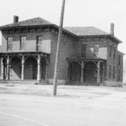 View of the John Kernan Mullen house at Lawrence and 9th (Ninth) Streets in the Auraria neighborhood of Denver, Colorado. The two-story brick house has a hip roof, chimneys, and covered porches.