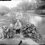 Outdoor portrait of Ida L. and Ernest L. Ballard with a Saint Bernard dog by the South Platte River in Denver, Colorado; costume includes knee pants, a sailor shirt, and a straw hat.