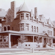A view a building with four porch entrances.  The sandstone row house features towers, bays, porches, recessed porches, transom windows, arches, stone chimneys and a carriage portico.