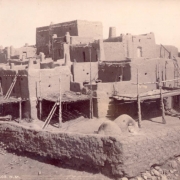 View of Native American (Taos) Taos Pueblo, New Mexico; shows adobe buildings with wood decks, adobe wall and ovens.