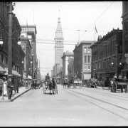 View northwest from California Street down 16th (Sixteenth) Street, Denver, Colorado; shows automobiles, horse-drawn wagons, delivery wagons & carriages, street railway car & tracks, Daniels & Fisher tower, streetlights with electric tramway cables, Stark street clock, pedestrians on sidewalk, Gano-Downs (721-739 16th & corner of Stout), A.T. Lewis & Son (800-818 16th & corner of Stout), May Company building.