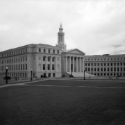 View of the City and County Building on Bannock Street in the Civic Center neighborhood of Denver, Colorado. Automobiles are parked near the building. Civic Center Park is nearby.