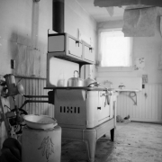 Interior view of the kitchen in Charles H. Harris (ranch homesteader) in Carbondale, Roaring Fork River Valley, Garfield County, Colorado; includes an enameled cook stove with kettles on top, a crock with  a decorative leaf pattern, meatgrinder (?), and wood panel wainscot.