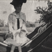 Mae Woodward poses in a hammock outdoors with her children probably in Colorado. She wears a hat decorated with feathers.