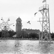 Men dive into Lake Rhoda at Lakeside Amusement Park in Lakeside (Jefferson County), Colorado; the casino tower and a ferris wheel are in the background.