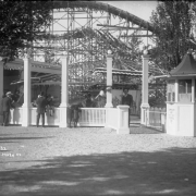 View of a ticket booth and roller coaster at Lakeside Amusement Park in Lakeside (Jefferson County), Colorado; people stand by railings.