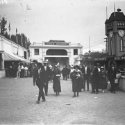 View of Lakeside Amusement Park in Lakeside (Jefferson County), Colorado; people walk by a clock tower and attractions with signs: "Thirty Third Degree" and "Lake Shore Railroad."