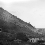 View of Eldorado Springs, Colorado, a spa founded by the Fowler family in 1904. The New Eldorado Hotel, a hipped-roof building with a veranda across the front, is on the hill above the valley; other buildings and small cottages are scattered on the hills around the resort.