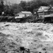 Houses line the banks of the South Boulder creek with the flood waters raging. One room of a house hangs out over the creek.