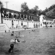Swimmers and onlookers are at the pool in Eldorado Springs, Colorado. A sign near the pool reads: "Warning Bathers Are Not Allowed To Use Pool Except When Life Guards Are On Duty."