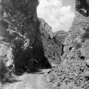 Sheer rock walls rise on either side of a dirt road in Eldorado Springs, Colorado. Buildings are on top of the hill in the distance.