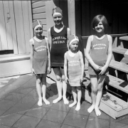 Four young girls stand in their swim apparel at the resort in Eldorado Springs, Colorado. Three of the girls wear swim caps, and their bathing suits has "Eldorado Springs," printed on the top section.