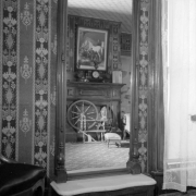Interior view at the Healy House Museum in Leadville (Lake County), Colorado; shows a mirror, ornate wallpaper, and the reflection of a fireplace, clock, a painting of a horse, a spinning wheel and a footstool.