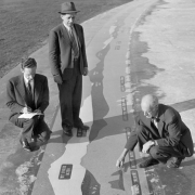 Men examine a panoramic mountain index at Cranmer Park in the Hilltop Neighborhood of Denver, Colorado; mountain names and elevations are rendered in stone tile.