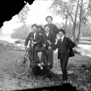 Outdoor portrait of men with a bicycle and bottles of beer possibly near the South Platte River in Denver, Colorado. They wear suits, bowties, and wide-brimmed hats.